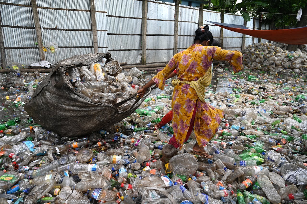 A worker in Chattogram sorts plastic bottles amidst a sea of waste, showcasing recycling efforts.