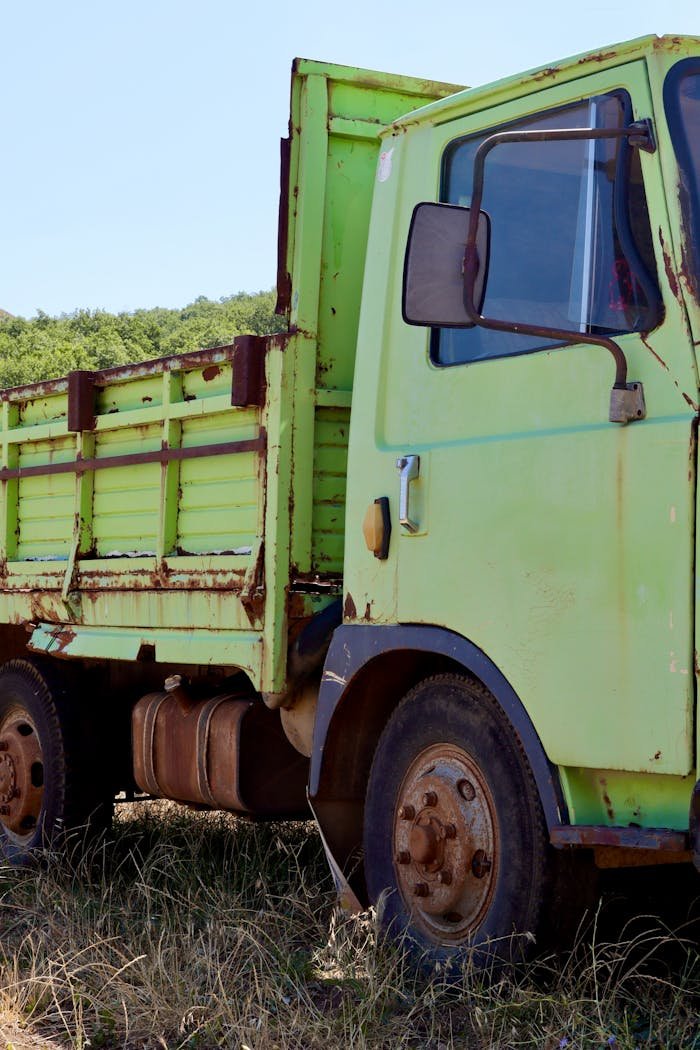 Vintage green truck with rust in a grassy field under clear sky, evoking nostalgia.
